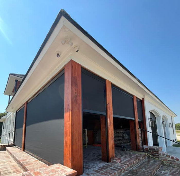 Motion screens installed on a covered patio with brick columns for shade and outdoor comfort in Lafayette, Louisiana